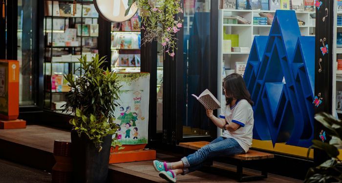 woman sitting in front of bookstore with big windows reading a book