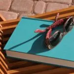 Image of a book beneath sunglasses and on a beach chair