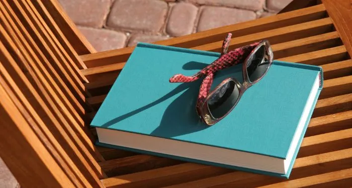 Image of a book beneath sunglasses and on a beach chair