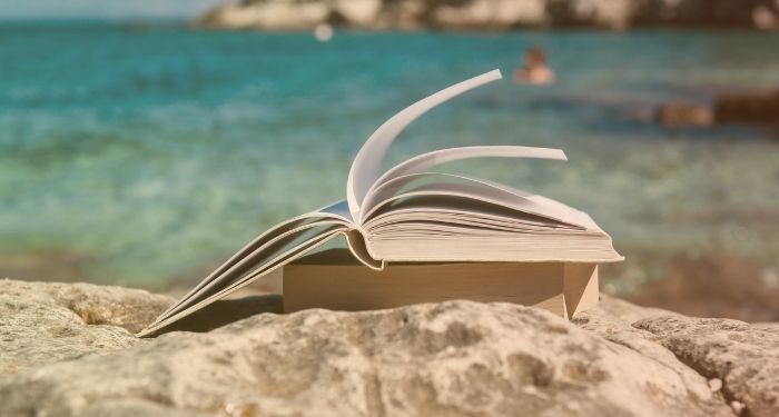 book splayed open on top of other book on beach with ocean behind