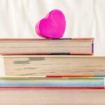 stack of books with the edges facing forward and a pink paper heart resting on top