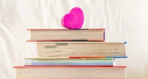 stack of books with the edges facing forward and a pink paper heart resting on top