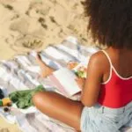 brown-skinned Black woman reading a book at the beach