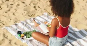 brown-skinned Black woman reading a book at the beach