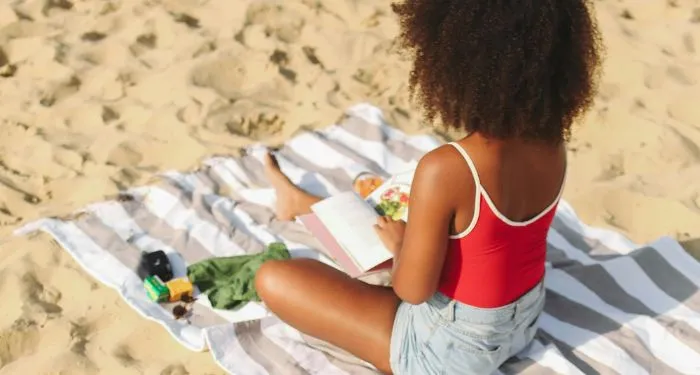 brown-skinned Black woman reading a book at the beach