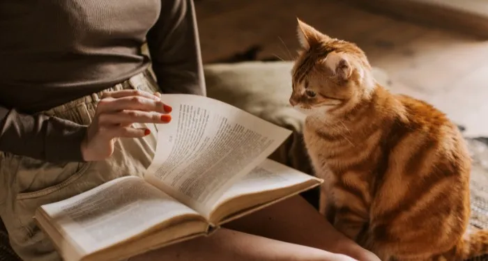 a photo of someone reading with a cat beside them