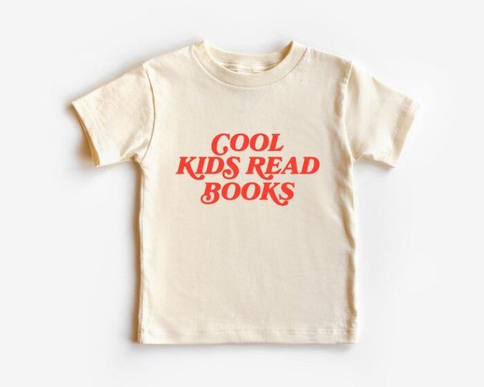 an ivory colored tshirt in toddler dimensions with bold red capitals reading "Cool Kids Read Books."