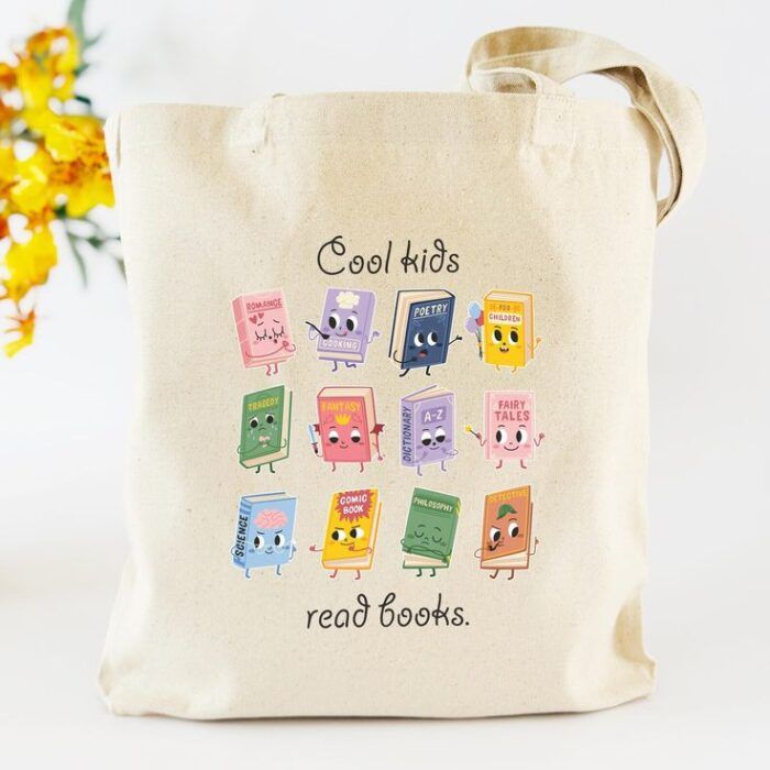 a beige tote bag with primary and pastel colors. Black letters read "cool kids read books," and personified books are displayed in a grid pattern.