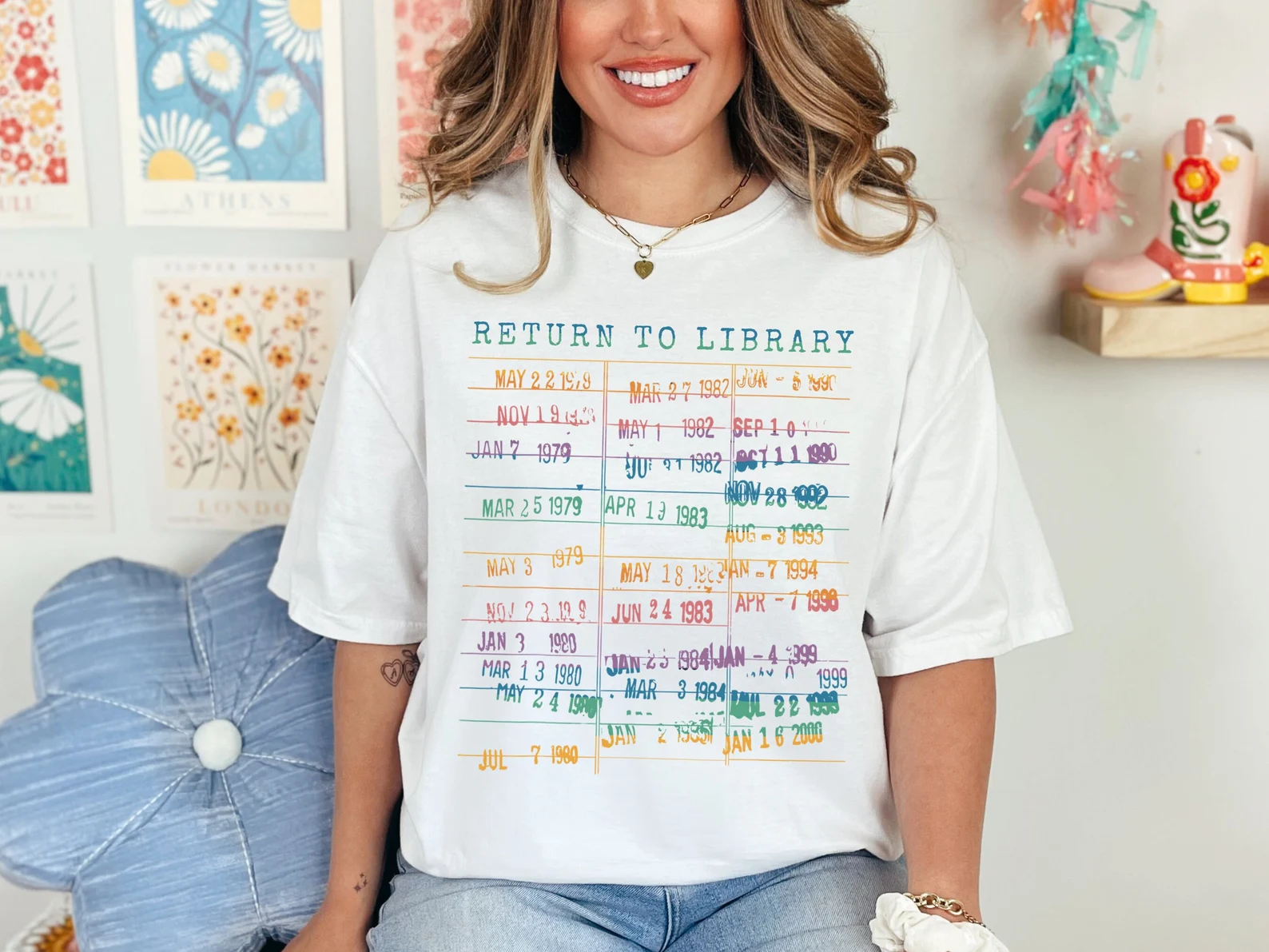 Image of a white t-shirt with a library due date card image. It says "return to library" at the top. All of the due dates on it are in rainbow colors. 