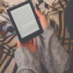 fair skinned woman reads ebook on throw blanket with coffee and dessert