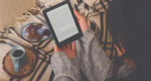 fair skinned woman reads ebook on throw blanket with coffee and dessert