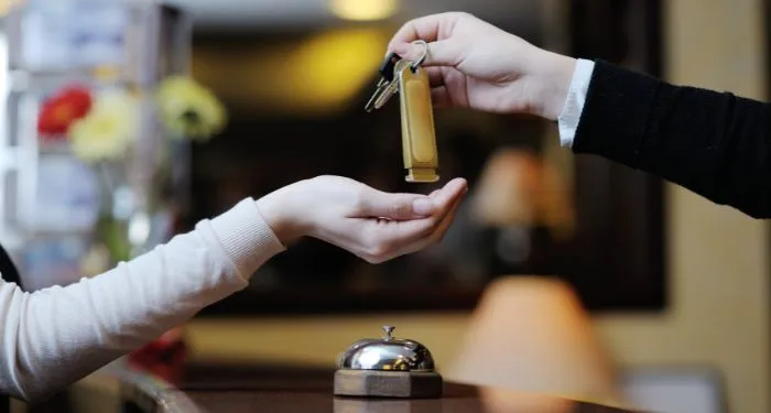 two hands exchanging a key in a hotel lobby/reception area