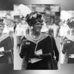 black and white image of Marsha P Johnson wearing a black velvet dress and a white feather in her hair