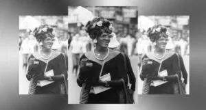 black and white image of Marsha P Johnson wearing a black velvet dress and a white feather in her hair