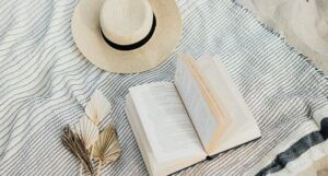 a sun hat, a book, and some origami plants on a blanket at the beach