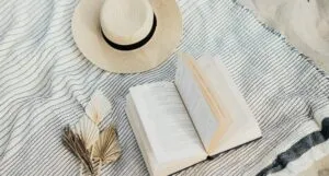 a sun hat, a book, and some origami plants on a blanket at the beach