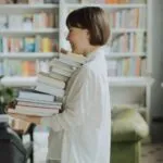 fair-skinned Woman in White Long Sleeve Shirt Carrying a Stack of Books More info Share