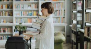 fair-skinned Woman in White Long Sleeve Shirt Carrying a Stack of Books More info Share