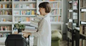 fair-skinned Woman in White Long Sleeve Shirt Carrying a Stack of Books More info Share