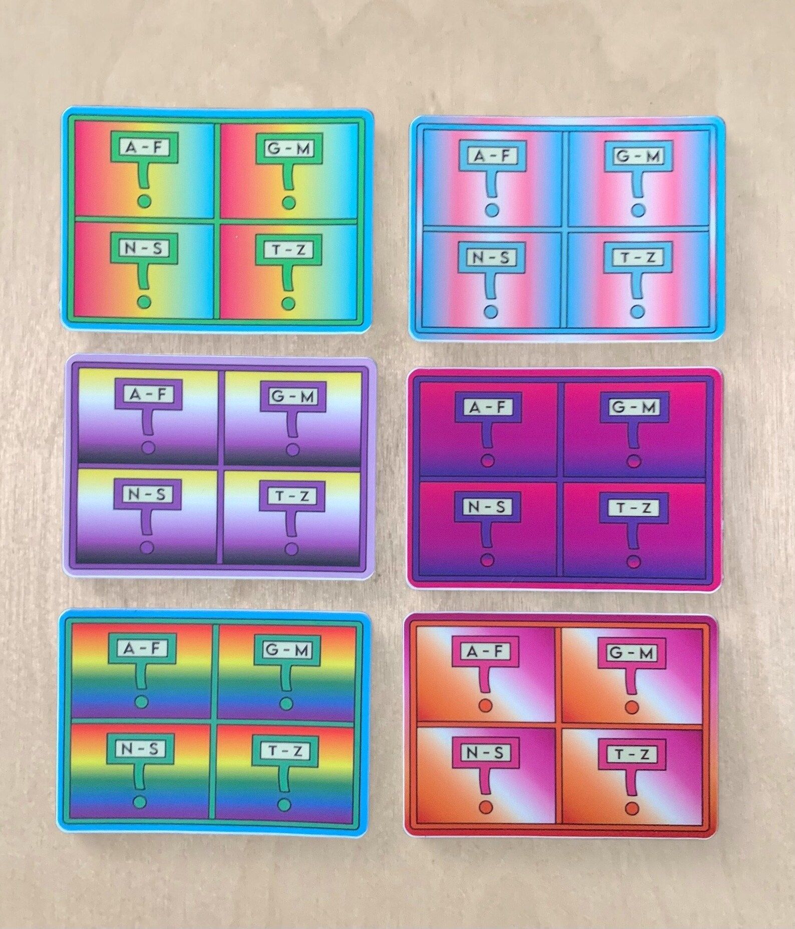 Image of a library card catalog sticker. Each of the stickers is done in a color palate representing different queer identities. 