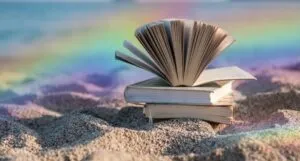 a stack of books on the beach with a rainbow gradient in the background