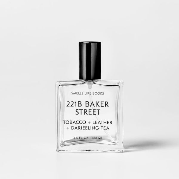 a clear glass perfume bottle with black text that reads Smells Like Books: 221B Baker Street - Tobacco + Leather + Darjeeling Tea