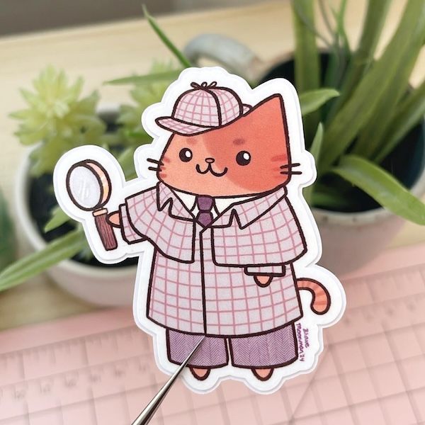 a sticker of a cat in a tweed coat and cap holding a magnifying glass resembling Sherlock Holmes