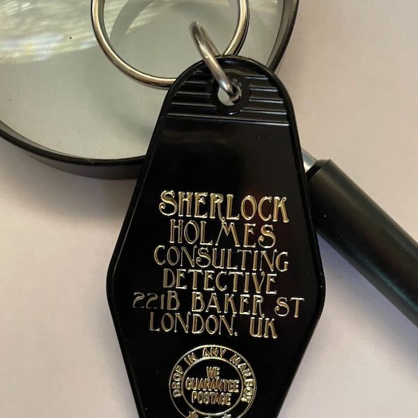 a black vintage motel key fob with gold text that says Sherlock Holmes Consulting Detective 221B Baker Street London, UK