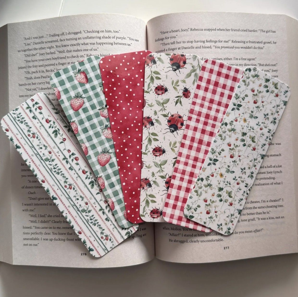 Image of six picnic-themed bookmarks with berries, ladybugs, and picnic blanket patterns displayed on a book