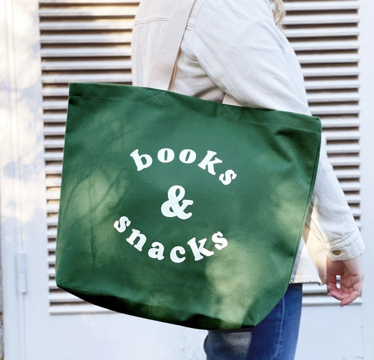 Image of someone carrying a large green tote with white text that says "books & snacks"