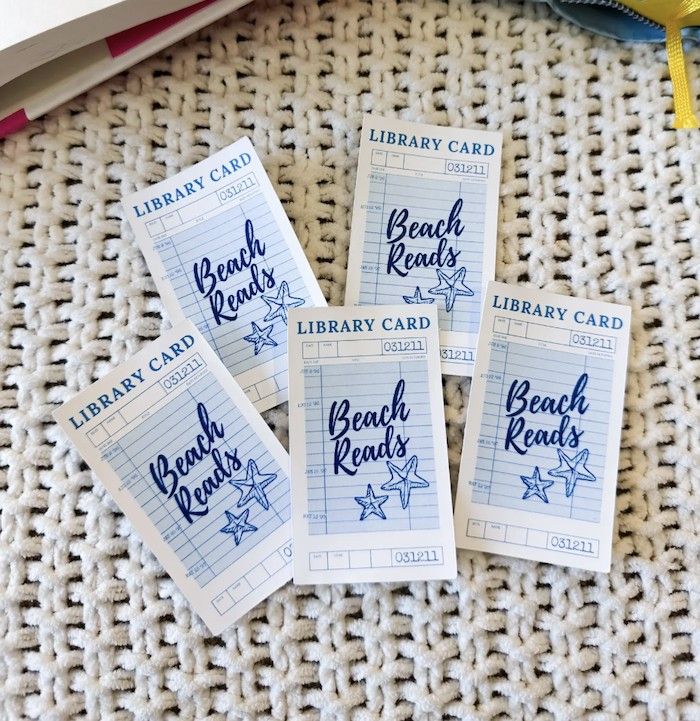 Pegatinas azules y blancas similares a los accesorios de catálogo de tarjetas de biblioteca y "Lecturas de playa" Una letra en el medio en la fuente.