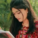 a young, fair-skinned Asian woman in brilliant red traditional clothing reading a book outside