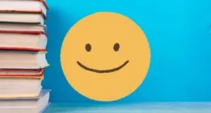 big yellow smiley face next to stack of books against blue background