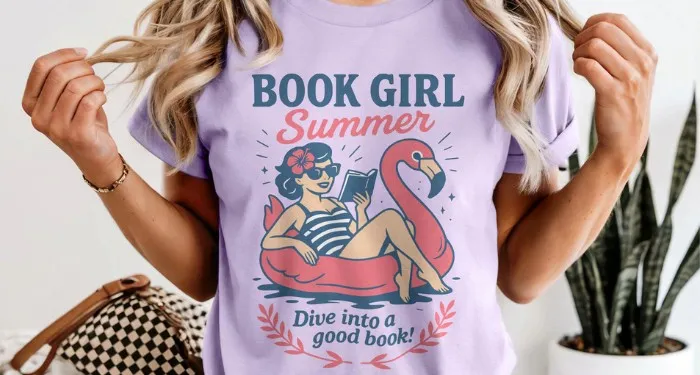 A purple t-shirt that reads 'Book Girl Summer' and 'Dive into a good book' alongside an image of a woman reading while floating on a flamingo tube.
