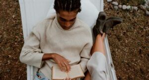 brown-skinned Black man with cornrows reading in a hammock beside someone with fair skin