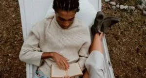 brown-skinned Black man with cornrows reading in a hammock beside someone with fair skin