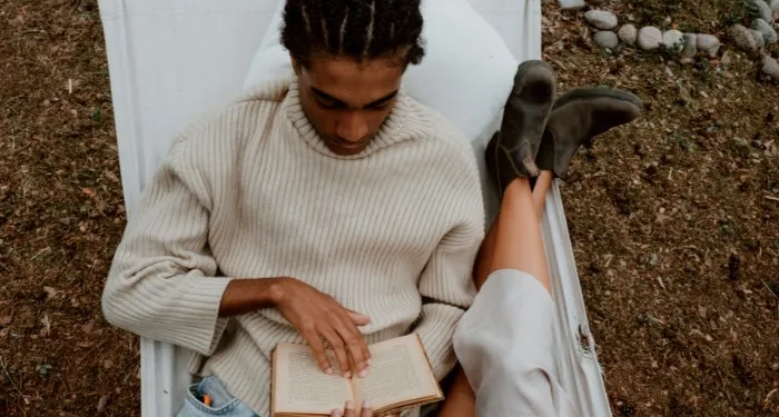 brown-skinned Black man with cornrows reading in a hammock beside someone with fair skin