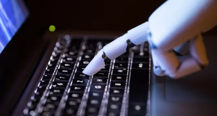 closeup of a robot's finger pressing a key on a laptop keyboard