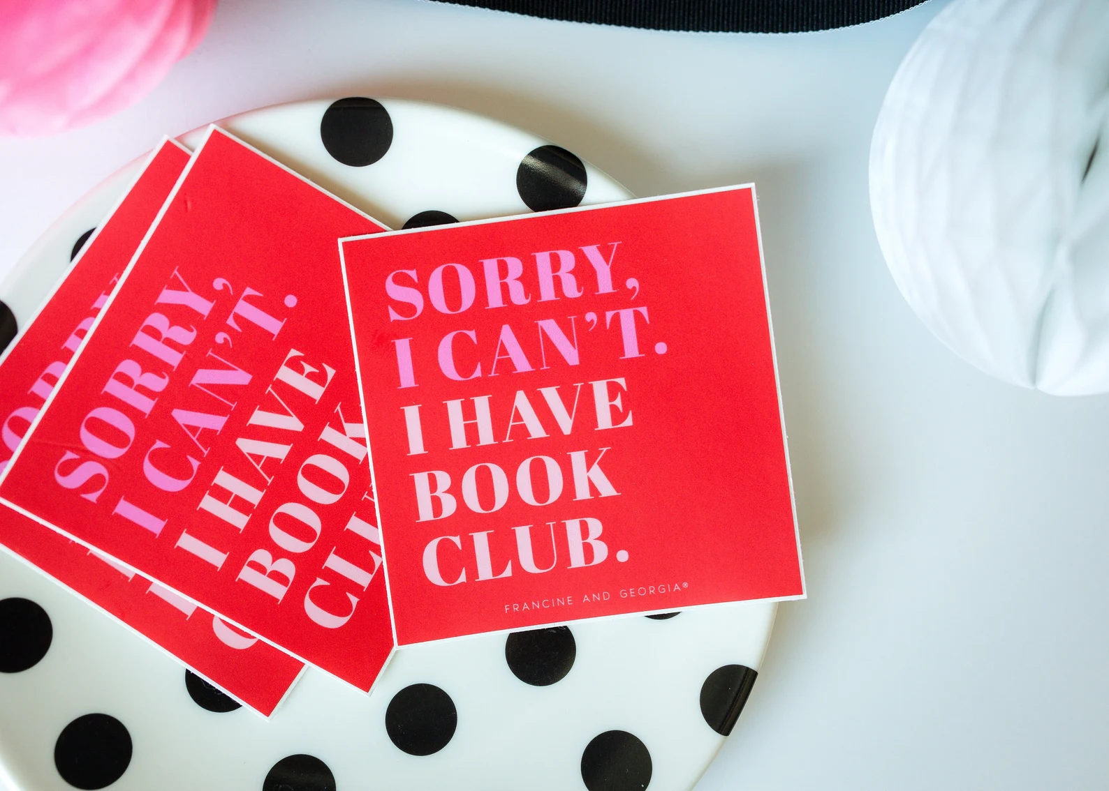 Image of several square stickers on a white and black polka dotted dish. The stickers are red, with pink and white font, that reads "Sorry, I can't. I have book club."