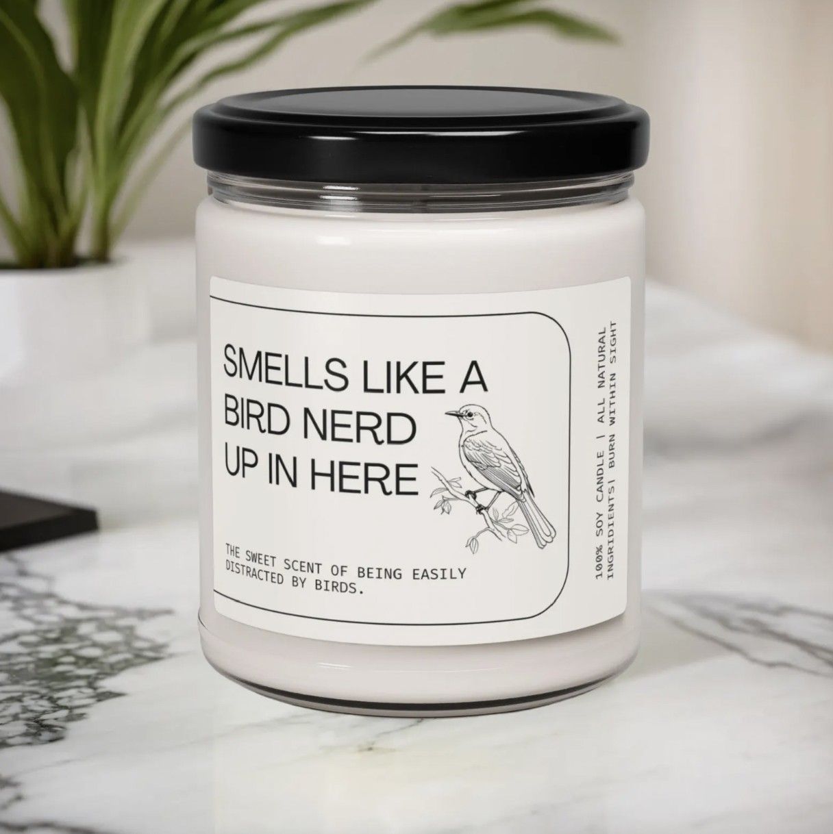 Image of a candle in a glass jar with a label that says "smells like a bird nerd up in here"