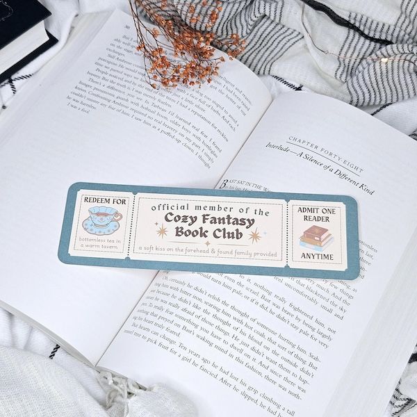 Un lugar diseñado para parecer un boleto de tren en un libro abierto. Él dice "Miembro oficial de Cozy FantasyBook Club" Con paneles laterales en el centro "Úselo para el té sin fondo" Y "Acepta siempre a un lector"