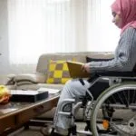 Image of a disabled person with a pink head scarf reading a book in their living room