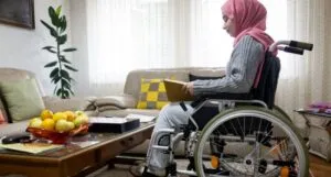 Image of a disabled person with a pink head scarf reading a book in their living room