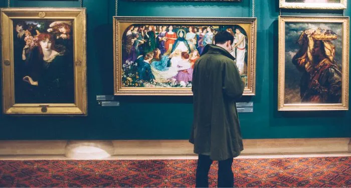 a person in a trench coat standing in front of a wall of paintings at a museum