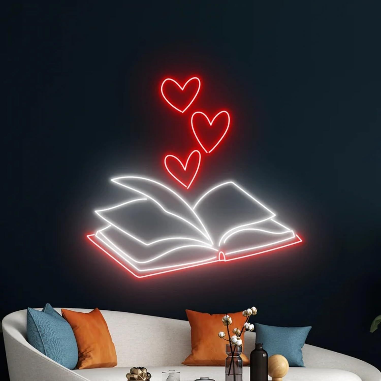 Image of a neon sign featuring an open book above a couch. The open book has red hearts coming out from its pages. 