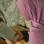a tan-skinned girl in a pink hijab reading a book
