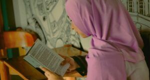 a tan-skinned girl in a pink hijab reading a book