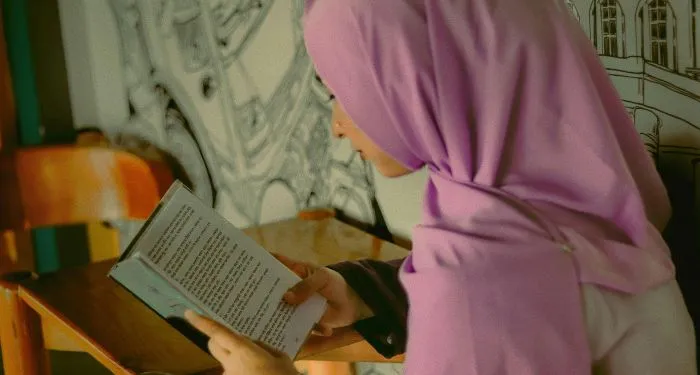 a tan-skinned girl in a pink hijab reading a book