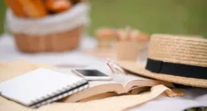 Picnic accessories, a smartphone, a book, and straw picnic hat on a white picnic blanket