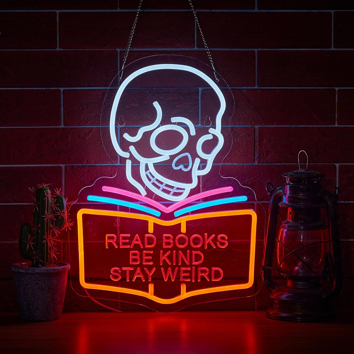 Image of a neon sign featuring a skull. It is behind an open book, with the words "read books, be kind, stay weird" on the book cover.
